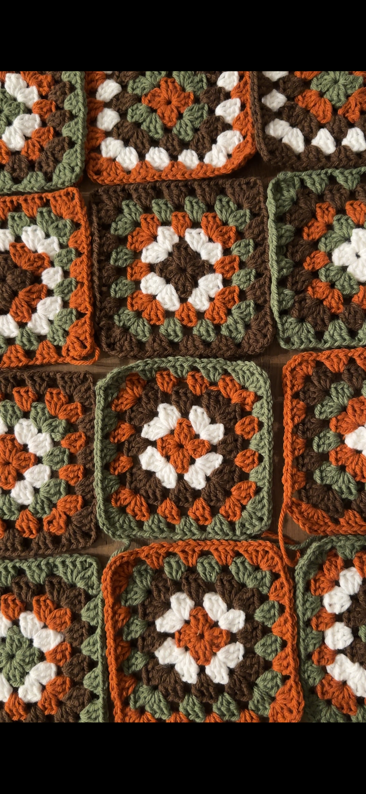A granny square in sage, cream and dusty pink yarn with a crochet hook